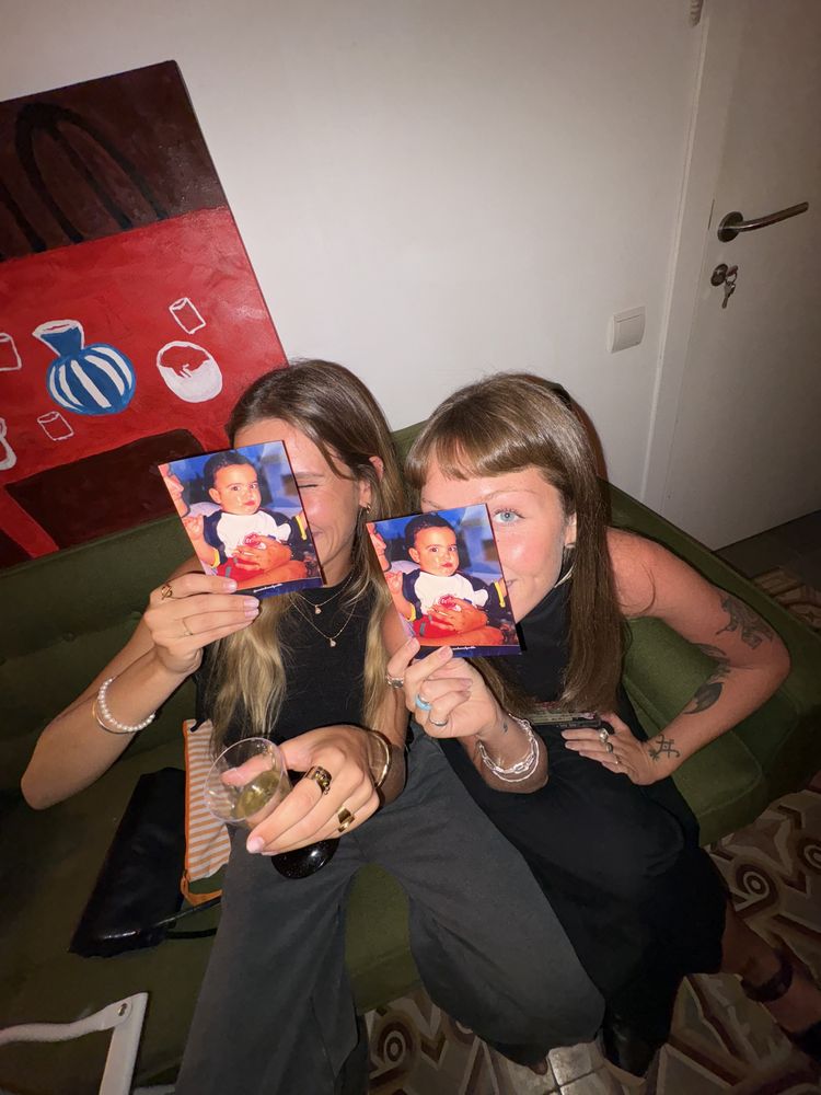 Dos invitadas tapándose la cara con cartas del bebé de la marca